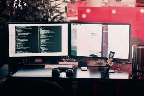 A desk with two monitors, keyboard, mouse, and phone.